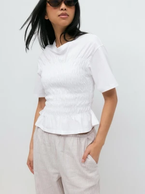 Vit smockad topp - Säljer en vit topp med smockad midja och volangkant nedtill. Toppen har korta ärmar och rund halsringning, vilket ger en söt och trendig look. Perfekt att styla med både jeans och kjol för en fräsch outfit.