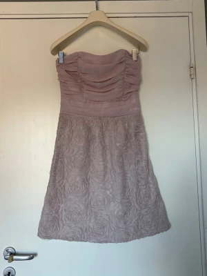 Ljusrosa axelbandslös kortklänning - Söt axelbandslös klänning i ljusrosa med draperad överdel och rosformad struktur på kjolen. 