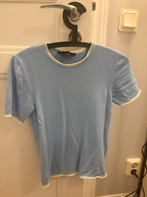 Ljusblå topp från Zara med kontrastsömmar - Säljer en ljusblå topp från Zara med korta ärmar och kontrastsömmar i ljusgul vid hals, ärmslut och nederkant. Toppen har en enkel, rak passform och är tillverkad i mjuk bomull. Perfekt för en avslappnad och trendig look.