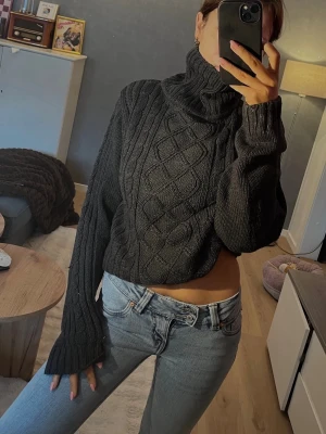 Mörkgrå stickad polotröja - Säljer en mörkgrå stickad polotröja med grovt flätmönster framtill. Tröjan har oversized passform, långa ärmar och hög polokrage som ger en riktigt mysig känsla. Man kan ha den som oversize eller vika upp den som på bild 1. Vintage från märket esmara. Storlek m 