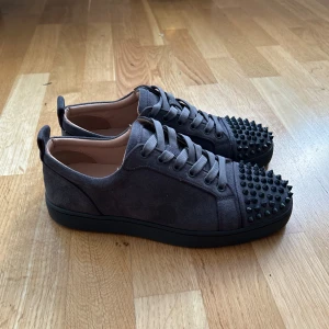Christian Louboutin Red bottoms gråa. - Snygga grå sneakers i mocka från Christian Louboutin med svarta nitar på tån och den ikoniska röda sulan. Skorna har endast använts ett fåtal gånger och är i mycket bra skick. Skorna är storlek 40 men passar dig som har 40-42 eftersom dom är gjort i ett töjbart material och anpassar sig enkelt efter dina fötter. 