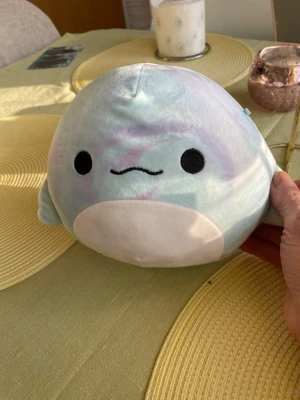 Squishmallows blå pastell säl - Supersöt och mjuk Squishmallows säl i blått och pastellfärger med vitt ansikte och mage. Rund form och broderat ansikte med svarta ögon och liten mun. Perfekt som gosedjur eller dekoration i rummet.19cm höjd
