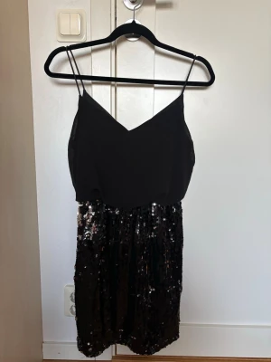 Svart paljettklänning  - Snygg svart kortklänning med v-ringad urringning. Kjoldelen är täckt av glittriga paljetter som ger en festlig look. 