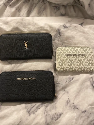 Svart och vit plånbok Michael Kors, YSL - Snygg plånbok från Michael Kors i svart och vitt med MK-logga över hela ytan. Plånboken har dragkedja runtom, flera fack för kort och myntfack med dragkedja. Perfekt för att hålla ordning på dina kort och kontanter. Öppen för prisförslag 