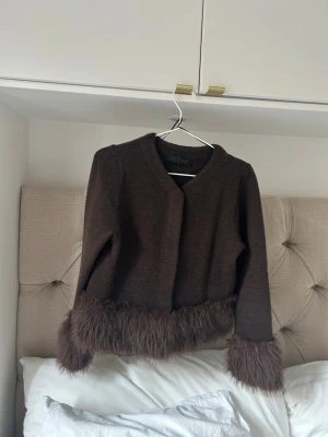 Brun cardiganjacka med fuskpälsdetaljer - Snygg brun cardiganjacka från Zara med fuskpälsdetaljer vid ärmslut och nederkant. Jackan har en rak och kortare passform, rund halsringning och är perfekt för att ge din outfit en trendig touch.