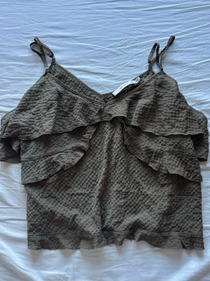 Grön volang topp med smala band - Säljer en snygg grön topp med smala axelband och volangdetaljer framtill. Toppen har en strukturerad, lite bubblig yta 