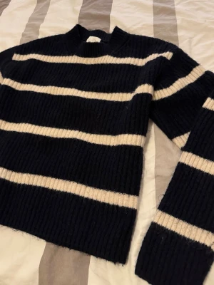 Svartvit randig stickad tröja - Mysig stickad tröja med breda svarta och vita horisontella ränder. Tröjan har en rak passform, rund halsringning och långa ärmar. Perfekt för dig som gillar klassiska mönster och vill ha något bekvämt och stilrent i garderoben.