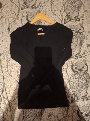 Svart ribbad långärmad topp - En svart, ribbad långärmad topp med v-ringning. Enkel och stilren design som passar till det mesta. Tillverkad i mjukt material för en bekväm känsla. Perfekt att matcha med jeans eller kjol.