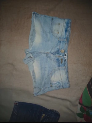 Ljusblåa jeansshorts från Sinsay - Snygga ljusblå jeansshorts från Sinsay med slitna detaljer och klassiska fickor både fram och bak. Shortsen har råa kanter nertill för en trendig look. Perfekta för varma dagar och enkel att matcha med allt.