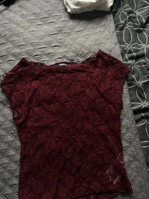 Vinröd spetsblus från Gina Tricot - Vinröd blus i spets från Gina Tricot med blommigt mönster. Modellen är croppad och ärmlös, perfekt för att lyfta en outfit. Toppens spets ger en romantisk vibe och den sitter snyggt figurnära.