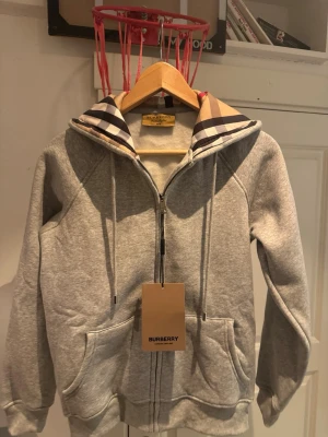 Burberry Hoodie - Grå Burberry hoodie Storlek M, med den klassiska burberry trycket i luvan. Super skön innuti.