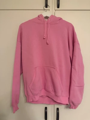 Bik Bok - En oversized hoodie i en härlig rosa färg med stor känguruficka framtill och justerbar huva med dragsko. Tillverkad i mjukt sweatshirtmaterial och har ribbade muddar vid ärmslut och nederkant. Perfekt för en chill och avslappnad stil.