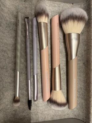 Sminkborstar från FLEAR - Hel nytt set med fem sminkborstar från FLEAR! Borstarna har syntetiska borst och handtag i beige, rosa och grå toner. Perfekta för applicering av puder, foundation, ögonskugga och bryn.