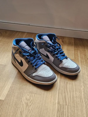 Nike Air Jordan 1 Mid grå/blå - Snygga Nike Air Jordan 1 Mid sneakers i grått och vitt med blå detaljer och blå skosnören. 