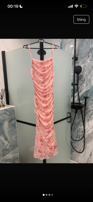 Rosa blommig långklänning med rynk - Säljer en långklänning i ljusrosa med blommigt mönster och tunna axelband. Klänningen har rynkade detaljer längs hela framsidan och baksidan för en smickrande siluett. Perfekt för sommarens alla tillfällen!