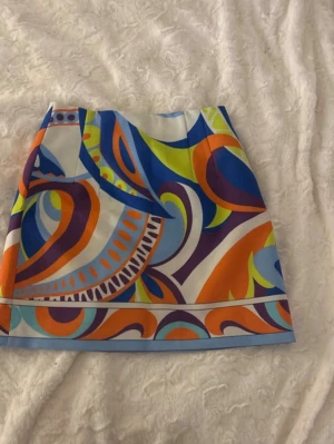 Färgglad kortkjol från Zara - Säljer en superfin kortkjol från Zara med färgstarkt abstrakt mönster i blått, orange, gult, lila och vitt. Kjolen har en rak passform och är tillverkad i ett slätt syntetmaterial. Perfekt för dig som vill sticka ut med en unik och lekfull stil! Dessutom aldrig använts 