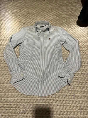 Randig skjorta från Ralph Lauren - Klassisk skjorta med blå och vita smala ränder från Ralph Lauren. Den är i bra skick. Passar xs eller mindre.
