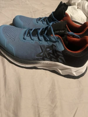 Blå sneakers från RYKA - Snygga blå sneakers från RYKA med svart och rödbrun detalj runt hälen. Ovandelen är i mesh för bra ventilation och sulan är grovt mönstrad i svart och vitt för extra grepp. Perfekta för dig som gillar sportig stil och komfort Helt oanvända