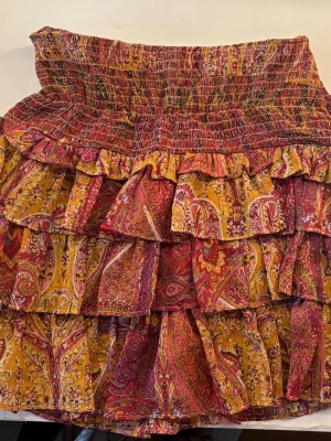 Mönstrad volangkjol från Zara - Färgstark kortkjol från Zara med volanger och paisley-inspirerat mönster i rött, gult och orange. Kjolen har bred smock i midjan och flera lager volanger som ger en bohemisk vibe. Perfekt för dig som gillar statement-plagg och vill sticka ut.