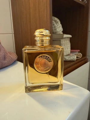 Burberry Goddess parfym guld - Burberry Goddess parfym i en elegant fyrkantig glasflaska med guldfärgat lock och detaljer. Flaskan har en exklusiv känsla med en rund guldplakett på framsidan där det står 'Burberry Goddess'. Perfekt för dig som gillar lyxiga dofter.