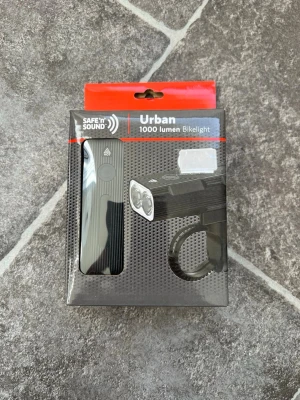 Safe'n'Sound Urban cykellbelysning 1000 lumen - Urban belysningset med framlampa och baklampa från Safe'n'Sound med 1000 lumen, svart aluminiumkropp och inbyggt batteri. Laddas via USB-C och är IP54-klassad samt stötsäker. Kan även användas som powerbank tack vare 2400mAh batteri. USB-C kabel medföljer.Köpt på cykel verkstad  för 399:- Oöppnad  Djur och rökfritt hem