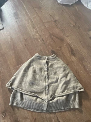 Grå cape-kofta med knappar - Stilren grå cape-kofta med knäppning framtill och ribbade kanter. Perfekt för lager-på-lager och ger en avslappnad men trendig look. Mjuk och skön, troligen i ull- eller bomullsblandning.