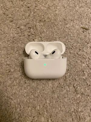 Apple AirPods Pro  - Säljer ett par vita Apple AirPods Pro med trådlöst laddningsetui. Hörlurarna har en stilren och kompakt design med silikonproppar för bra passform. Perfekta för musik, poddar och samtal. Laddningsetuiet är också vitt och har en LED-indikator på framsidan.