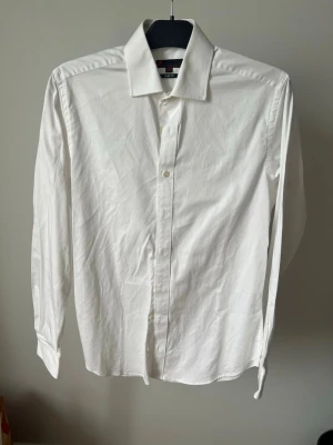 Vit klassisk skjorta från Dressmann - Klassisk vit skjorta från Dressmann med lång ärm och knappar framtill. Skjortan har en stilren design med slim fit passform och är tillverkad i bomull, perfekt för en clean och enkel look.