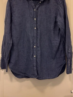 Blå skjorta från Boomerang - Säljer en stilren blå skjorta från Boomerang. Skjortan har klassisk krage, vita knappar framtill och långa ärmar med knapp vid manschetten. Perfekt för en avslappnad men snygg look.