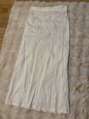 Vit långkjol från Nelly - Snygg vit långkjol från Nelly i enkel och stilren design. Kjolen har rak passform och är tillverkad i ett mjukt bomullsmaterial som känns skönt mot huden. Perfekt att styla med en crop top eller en oversized tröja. Man viker den även i toppen om man vill. 