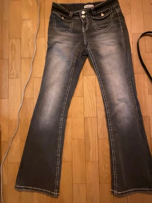 Bootcut jeans med ljusa slitningar - Snygga bootcut jeans i grå denim med ljusa slitningar framtill och markerade sömmar. Klassisk femficksmodell med dubbla knappar i midjan. Perfekta för dig som gillar en retro vibe och vill ha ett par jeans med lite extra attityd.