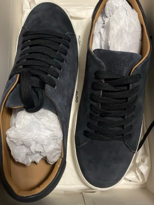 Mörkblå sneakers från ALDO - Stilrena mörkblå sneakers från ALDO med svart snörning och vit sula. Ovandelen är i mockaliknande material och insidan har en beige ton. Perfekta för dig som gillar en clean och modern look. Pris kan diskuteras 