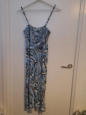 Mönstrad långklänning  - Långklänning från Anna Field med smala axelband och ett färgstarkt abstrakt mönster i blått, svart och vitt. Klänningen har smock upptill och är tillverkad i ett lätt och bekvämt material. 🩷
