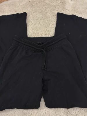 Svarta mjukisbyxor med dragsko - Svarta mjukisbyxor med resår och dragsko i midjan. Byxorna har raka ben och är tillverkade i ett mjukt och bekvämt tyg, perfekta för en avslappnad stil. Klassisk modell utan synliga loggor eller detaljer.