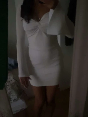 Vit klänning  - Säljer en vit klänning med v-ringad front och långa utsvängda ärmar. Klänningen har en figurnära passform och twistad detalj vid bysten. 
