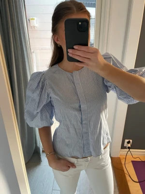 Blåvit randig blus med puffärm - Snygg blus med blå och vita vertikala ränder och puffiga korta ärmar. 