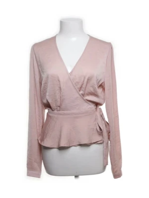 Ljusrosa omlottblus med knyt - Söt ljusrosa omlottblus med knyt i sidan och v-ringad hals. Blusen har långa ärmar och en lätt volang nedtill som ger en feminin siluett. Tillverkad i ett mjukt, tunt material som faller snyggt.