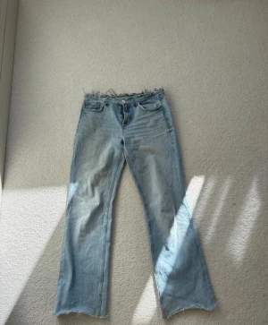 Ljusblåa lågmidjade jeans - Ljusblå jeans med raka ben och råa, fransiga kanter både i midjan och vid bensluten. Klassisk femficksmodell i denim med dragkedja och knapp. Perfekta för en avslappnad och trendig look. Står inte storlek men skulle säga 36-38