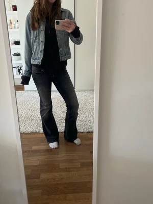 Ljusblå klassisk jeansjacka - Säljer en ljusblå jeansjacka i klassisk modell med raka ärmar och två bröstfickor med lock och knappar. Jackan har en snygg tvättad denimlook och silverfärgade knappar framtill. Perfekt att slänga över en hoodie eller t-shirt för en avslappnad stil.