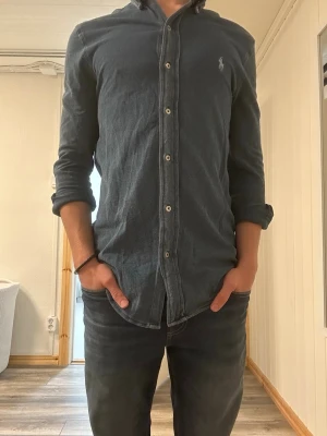 Mörkblå skjorta från Ralph Lauren - Säljer en mörkblå skjorta från Ralph Lauren med klassisk knappslå och broderad logga på bröstet. Skjortan har lång ärm, normal passform och är tillverkad i mjuk bomull. Perfekt för en stilren och avslappnad look.