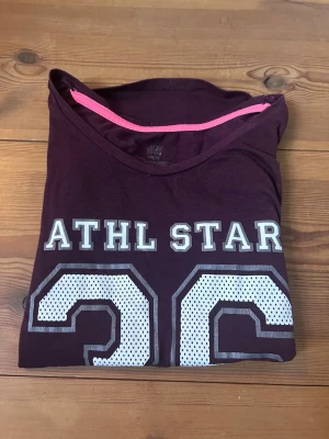 Vinröd sporttröja - Vinröd T-shirt med vitt tryck på magen. Knappt använd så i väldigt bra skick. Skriv om du har frågor!