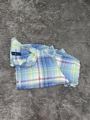 Cropped Polo Ralph Lauren Plaid Shirt - Superfin rutig skjorta från Ralph Lauren i härliga pastellfärger. Den här modellen är kortare (cropped). • Stil: Cropped / Kort modell • Detaljer: Klassisk broderad logga på bröstet. • Skick: Toppskick, inga anmärkningar. 