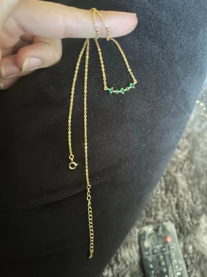 Guldhalsband med gröna pärlor - Snyggt och tunt halsband i guldfärgad metall med små gröna pärlor på rad framtill. Kedjan är enkel och har ett klassiskt lås samt förlängningskedja för justerbar längd. Perfekt för dig som gillar minimalistiska smycken med en färgklick.