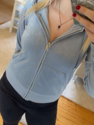 Ljusblå velour hoodie från Juicy Couture - Säljer en ljusblå hoodie i mjuk velour från Juicy Couture. Hoodien har dragkedja, fickor framtill, huva med snören och diskret Juicy Couture-logga broderad på bröstet. Perfekt för en chill och trendig look. Är lite trasig vid kedjan men de påverkar inget. 