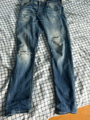 Blåa Jack and Jones jeans  - Säljer ett par blå slim glenn jeans från Jack and jones med  coola slitningar, de har används väldigt sparsamt, och är i str W31 L34 