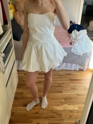 Vit axelbandslös jumpsuit med snörning - Supersöt vit axelbandslös jumpsuit med volangig kjoldel och snygg snörning i ryggen. Är i storlek L men passar M/S eftersom den går att knyta. Helt ny med lappen kvar!