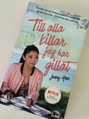 Till alla killar jag har gillat - Ungdomsroman av Jenny Han med ett färgstarkt omslag i pastellfärger. Boken har ett mjukt pocketformat och framsidan visar en tjej i rosa jacka som skriver i ett anteckningsblock. Perfekt för dig som gillar romantik och drama. Pocketform!