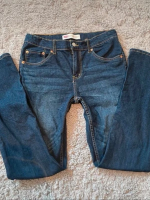 Levi’s jeans - Säljer ett par snygga Levi’s jeans som tyvärr inte kommer till användning längre. De är i mycket bra skick, utan fläckar eller slitage.  Jeansen är en slimmodell med mycket stretch, vilket gör dem extra bekväma och ger en fin passform. Det passar till det mesta i garderoben - både vardag och lite mer uppklätt.  Storleken motsvarar XS i vuxenstorlek. Hör gärna av dig vid frågor! 