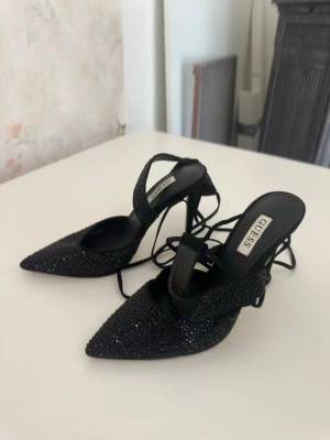 Guess klackskor stilett - Klackar från Guess. Använda en gång inhomhus. Supersöta. Svarta med glitter, alla stenar kvar! Storlek 36, normal i storlek. Knytband som knyts vid vristen. Nypris ca 1200kr.