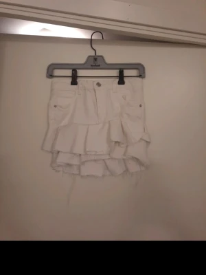 Vit volangkjol från Zara - Supersnygg vit kortkjol från Zara med volangdetaljer och råa kanter. Kjolen har fickor fram och bak samt knapp och dragkedja i midjan. Perfekt för dig som vill ha en trendig och unik look. Jag har sytt om skinnyjeans till en volangkjol.